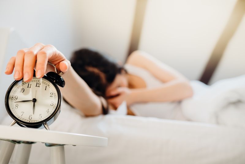woman covering face while turning off alarm clock at just before 6.45 in the morning