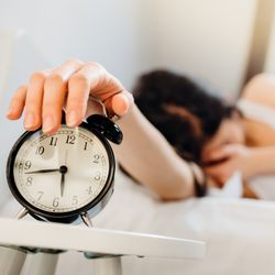 woman covering face while turning off alarm clock at just before 6.45 in the morning