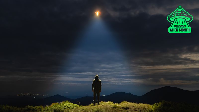 Person looking up at the sky, standing in the light of a UFO