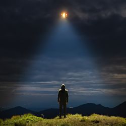 Person looking up at the sky, standing in the light of a UFO