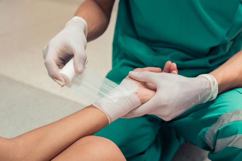 medical worker in green scrubs and white gloves applies bandage to patient's hand (close up shot)