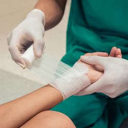 medical worker in green scrubs and white gloves applies bandage to patient's hand (close up shot)