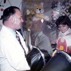 David Vetter, a young boy with dark hair, pictured inside the plastic sterile "bubble" in which he lived. Immunologist John R. Montgomery interacts with David via a glovebox.
