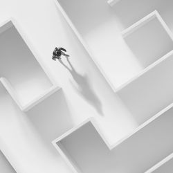 A photo of a male figure walking through a white maze. The image is looking down on the figure from above. His shadow is being cast in front of him as he walks through this white space.