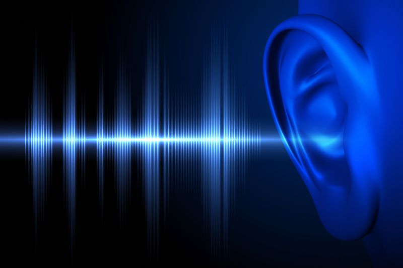 A digital image showing a close up of a human ear on the far right. There are sound waves represented as spiky lines of light entering the ear. Both the ear and the light consist of blue tones and both are set against a black background. 