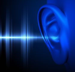A digital image showing a close up of a human ear on the far right. There are sound waves represented as spiky lines of light entering the ear. Both the ear and the light consist of blue tones and both are set against a black background. 