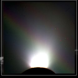 An image of the south pole of enceladus in shadow ith a geyser on the rim. Overalyed, a more distant image of the south pole with a wider view of the ice emission. A rainbow line is visible above the moon, from one side of the image to the next.