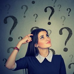 The photo shows a young woman wearing a dark top with a tick white collar looking up and scratching her head. She has a slightly confused look on her face. There are large question marks floating around her. 