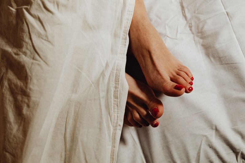 A woman's bare feet with red painted toenails in bed