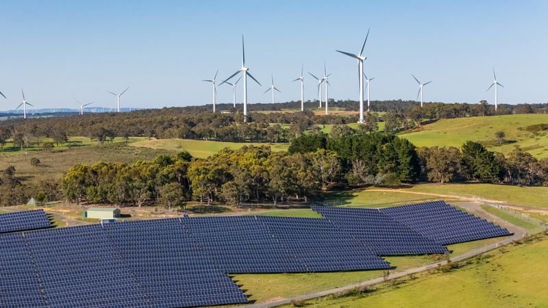 Aerial drone view of a hybrid solar and wind farm showing the large wind turbines in the background for renewable clean energy supply located at Bannister, NSW, Australia