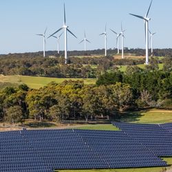 Aerial drone view of a hybrid solar and wind farm showing the large wind turbines in the background for renewable clean energy supply located at Bannister, NSW, Australia