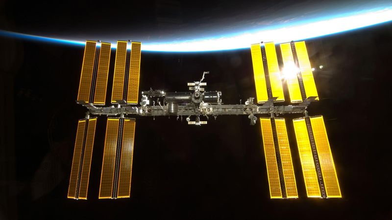 The iss against the limb of the Earth with sunlight reflected on its solar panels.