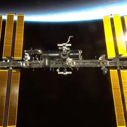 The iss against the limb of the Earth with sunlight reflected on its solar panels.