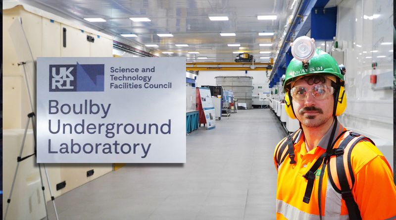 A photo of the lab, of Alfredo Carpineti (a white man with a dark hair and a moustahce) dressed in bright orange gears and the sign of the Boulby Underground Lab