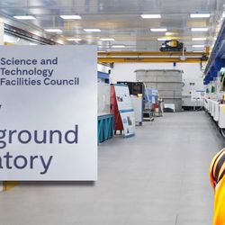A photo of the lab, of Alfredo Carpineti (a white man with a dark hair and a moustahce) dressed in bright orange gears and the sign of the Boulby Underground Lab