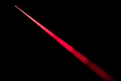 A close up photo of a red laser beam being fired through a dark space. The red beam cross through the photo from the top left to the bottom right, becoming slightly wider in the bottom corner. 