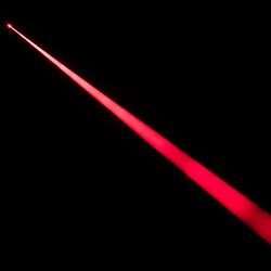 A close up photo of a red laser beam being fired through a dark space. The red beam cross through the photo from the top left to the bottom right, becoming slightly wider in the bottom corner. 