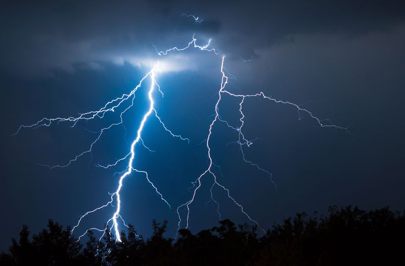two massive lightning strikes down to a dark forest against a dark blue sky