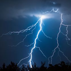 two massive lightning strikes down to a dark forest against a dark blue sky