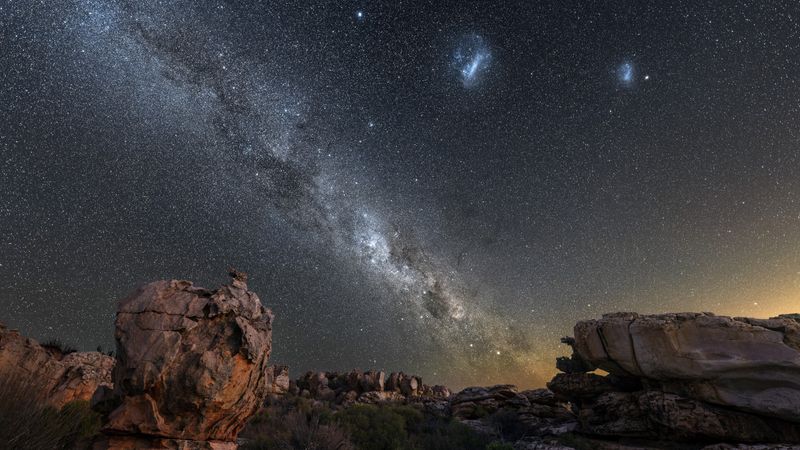 a picture of the night sky showing off a lot of stars, the milky way and the fuzzy magellanic clouds