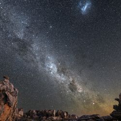 a picture of the night sky showing off a lot of stars, the milky way and the fuzzy magellanic clouds