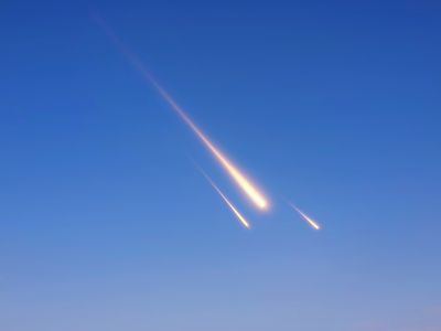 A photo showing three meteorites falling through the sky. They appear as three streaks of burning light set against a blue background. The largest meteorite is the closest, and the two behind it are progressively smaller. 