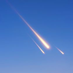 A photo showing three meteorites falling through the sky. They appear as three streaks of burning light set against a blue background. The largest meteorite is the closest, and the two behind it are progressively smaller.