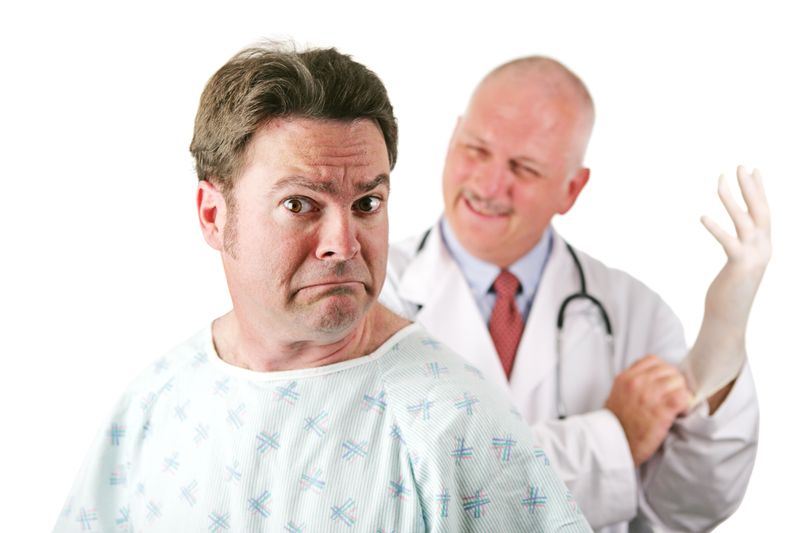 White male nervous-looking patient about to be examined by a smiling white male doctor who is putting a white medical glove. Isolated on white.