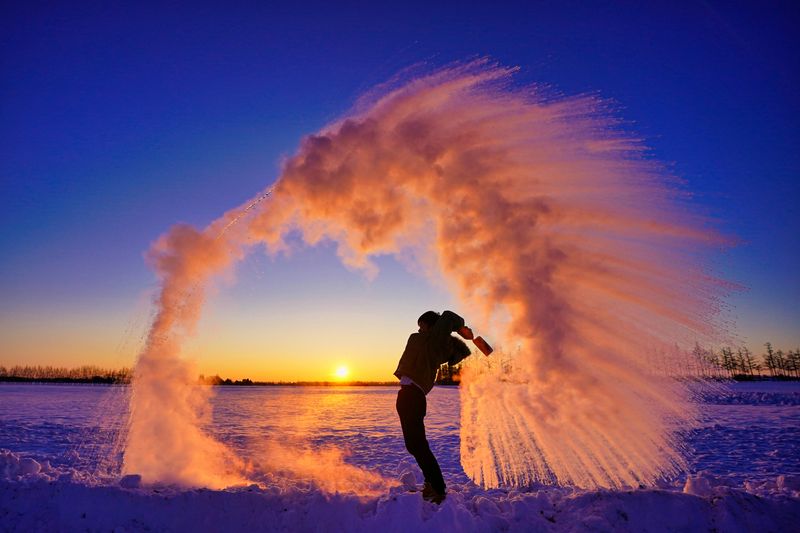 Photograph showing the Mpemba effect in action - someone is outside in the snow, throwing a pan of boiling water into the air, which is freezing immediately