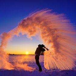 Photograph showing the Mpemba effect in action - someone is outside in the snow, throwing a pan of boiling water into the air, which is freezing immediately