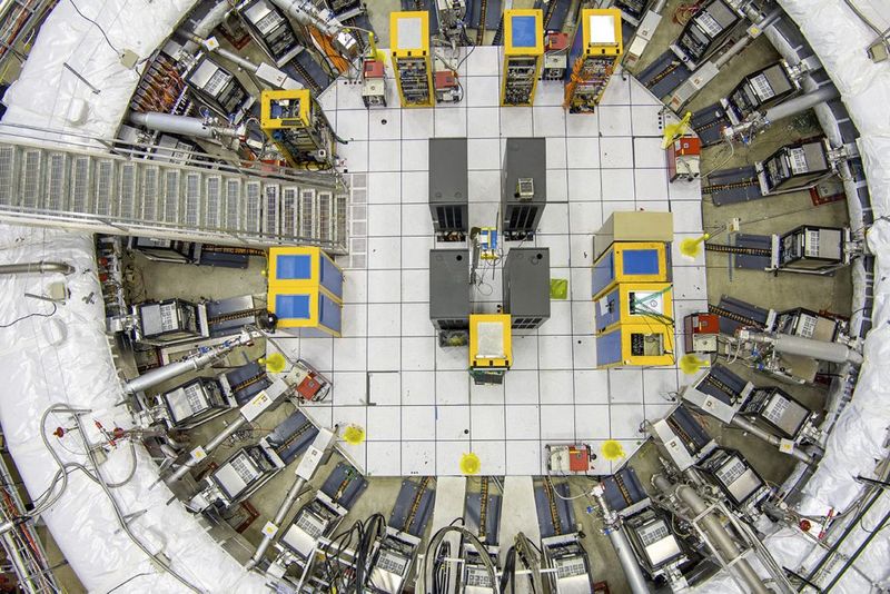 A partially visible ring covered in white is the accelerator. On one side is a metal staircase and many devices are visible inside the ring attached to the donut. 