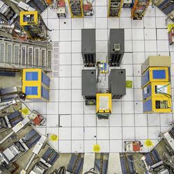 A partially visible ring covered in white is the accelerator. On one side is a metal staircase and many devices are visible inside the ring attached to the donut. 