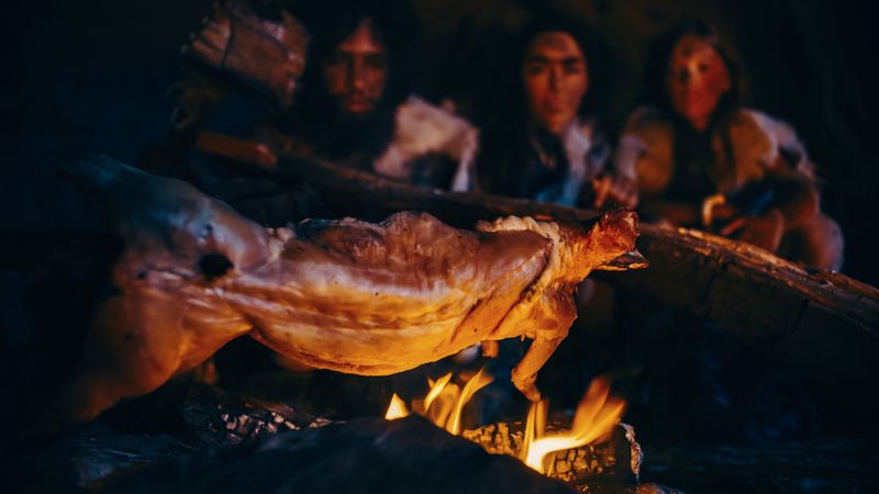 Neanderthals sat around a fire with an animal, maybe a deer, on a spit roast 