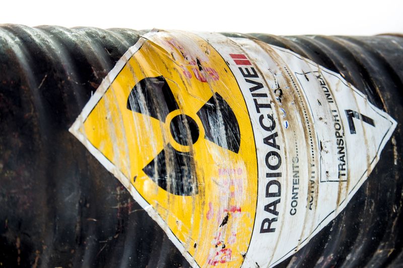 A photo of a canister of radioactive material on its side. The canister is black and ribbed, with a hazardous sign in the middle showing a radiation symbol. 