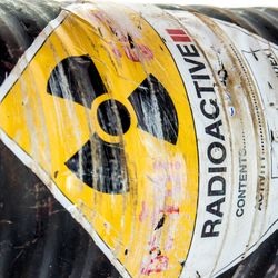 A photo of a canister of radioactive material on its side. The canister is black and ribbed, with a hazardous sign in the middle showing a radiation symbol. 