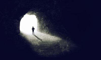 Man standing at cave entrance watching the light at the end of the tunnel