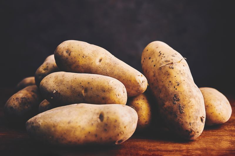 pile of potatoes on a wooden surface with a dark background