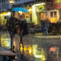 A couple walk through the city in the rain, with drips of water on the water.