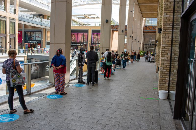 people queuing in a shopping centre in the UK after the national lockdown had started to lift in June 2020; they're standing on blue discs on the floor designed to enforce the 2-metre social distancing rules