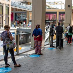 people queuing in a shopping centre in the UK after the national lockdown had started to lift in June 2020; they're standing on blue discs on the floor designed to enforce the 2-metre social distancing rules