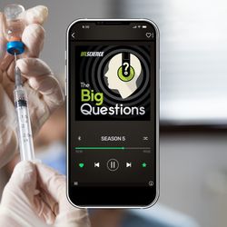 A smartphone showing season 5 of The Big Questions, on background of gloved hands inserting a needle into a vaccine vial