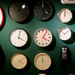 A group of clocks on a green wall.