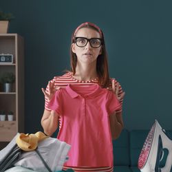 woman wearing glasses holding up a polo shirt that has shrunk in the wash