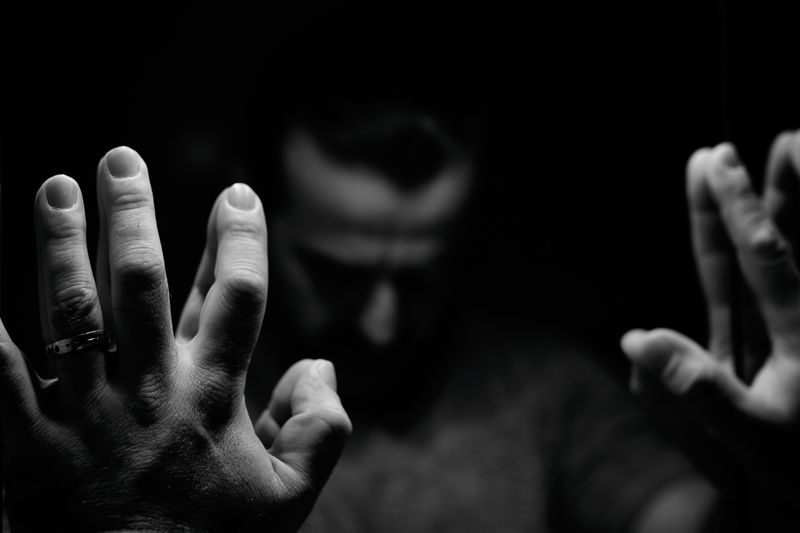 Man in despair with raised hands and bowed hand, monochromatic image in a low light room looking in front of mirror