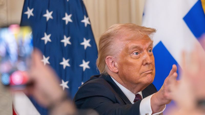 Donald Trump wearing a lot of foundation stares vacantly off camera as hand used phones to photograph him.