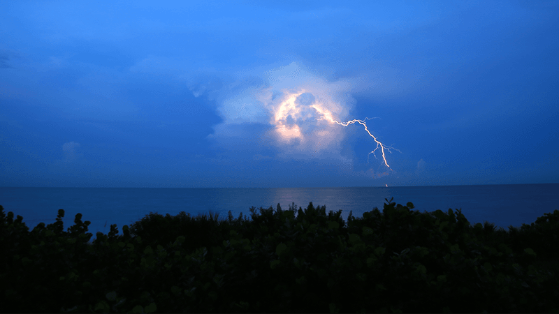 Lightning lighting up a cloud above the ocean.