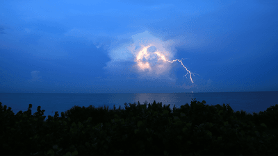 Lightning lighting up a cloud above the ocean.
