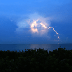 Lightning lighting up a cloud above the ocean.