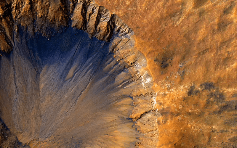 a crater with slopey channels and dark lines across the rocky landscape of mars.