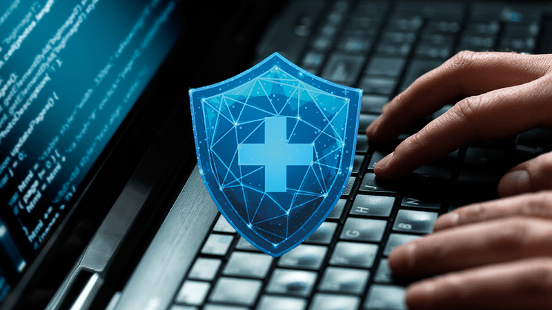 close up of hands on a laptop keyboard with some code on the screen, overlaid with a shield containing a cross to indicate health data